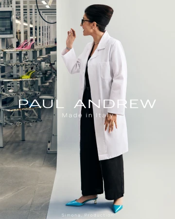 Woman in white lab coat and black trousers wearing bright blue pointed-toe heels against a white studio sweep backdrop.
