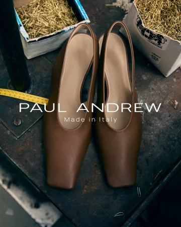 Brown leather slingback shoes resting on a dark metallic workbench in an Italian workshop setting.