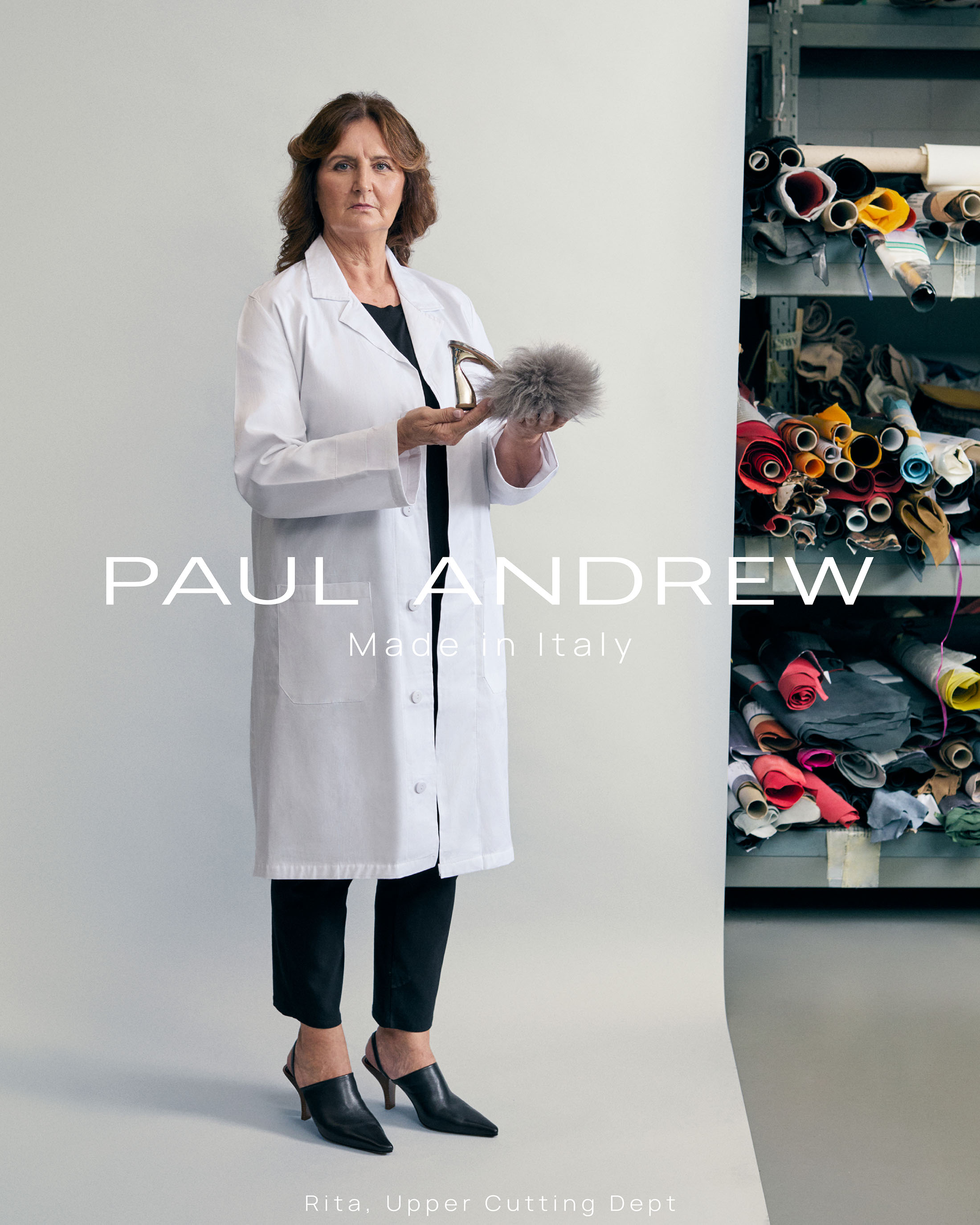 Woman in white lab coat holding a high-heeled shoe against a studio backdrop with fabric shelves.