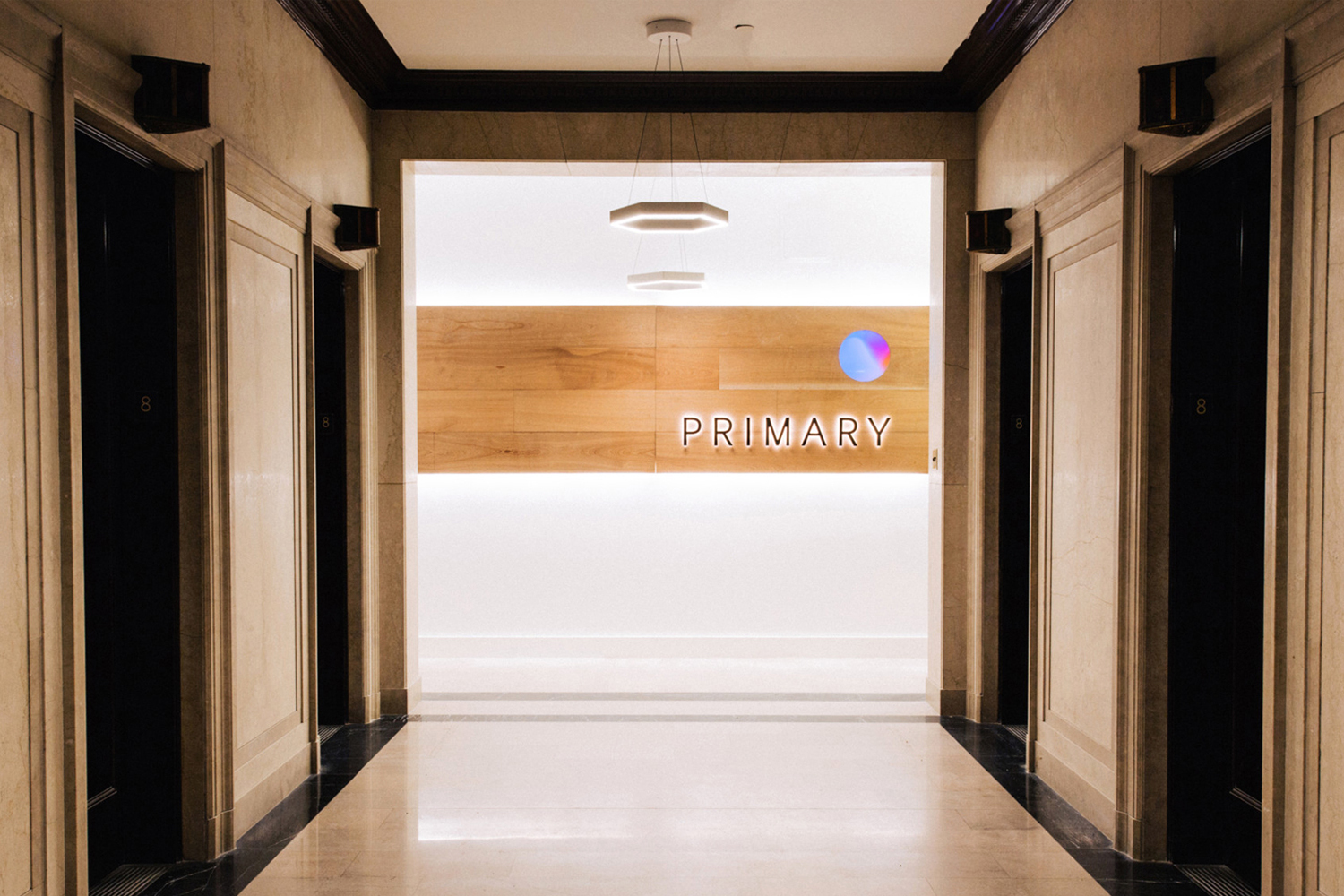 Interior hallway view featuring classic architectural paneling, black doors, and a central illuminated sign reading PRIMARY