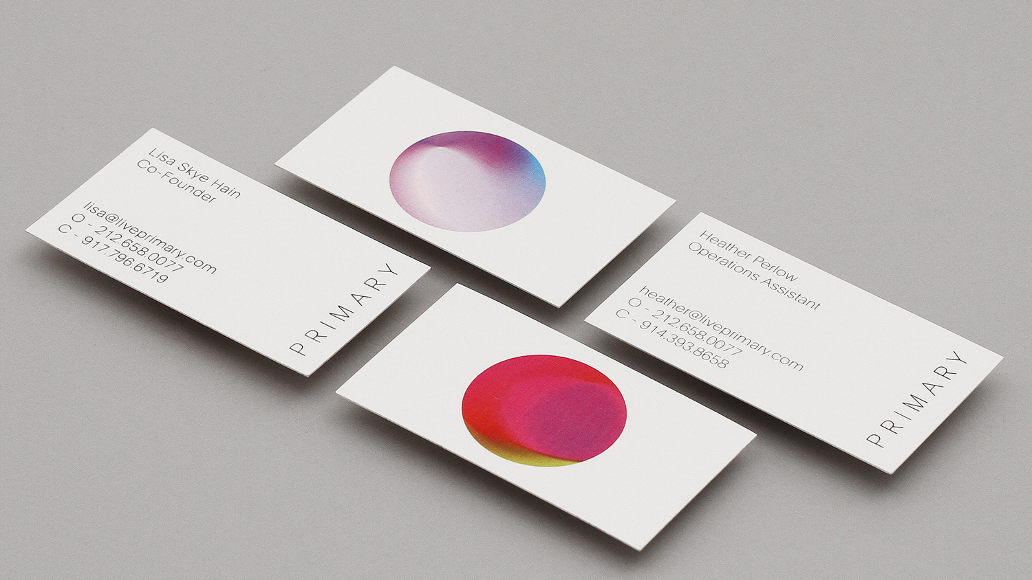 Four printed business cards featuring minimalist typography and colorful circular gradients on grey surface