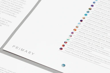 Close-up of printed brand identity document on white paper featuring the word PRIMARY and a list of amenities with circular color gradients.