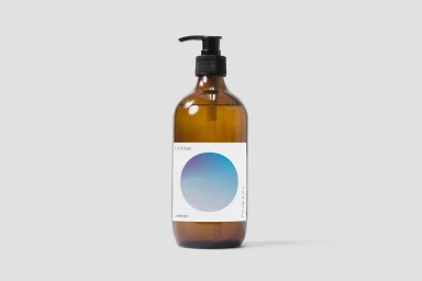 Amber glass pump bottle of hand soap with a white label featuring a blue and purple gradient circle on a plain light grey background.