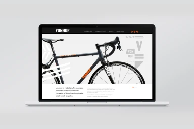 A laptop displaying a modern bicycle website with grey frame and orange typography against a clean light grey background