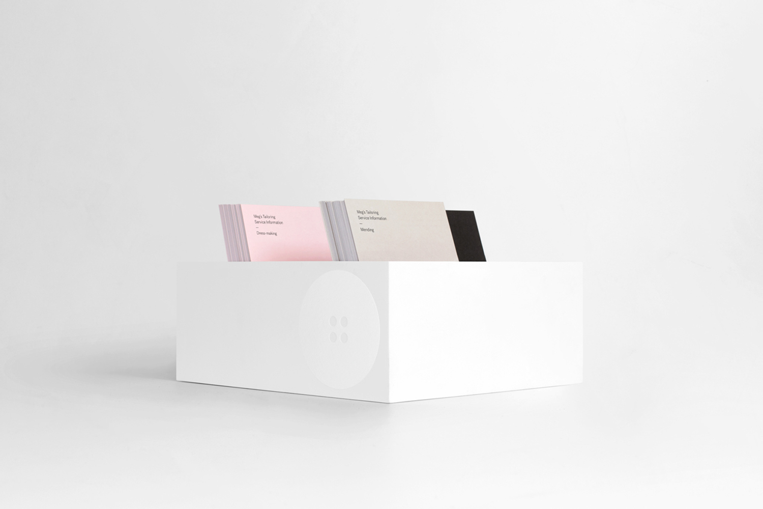White storage box holding stacked business cards in pink, cream, and black against a white seamless background.