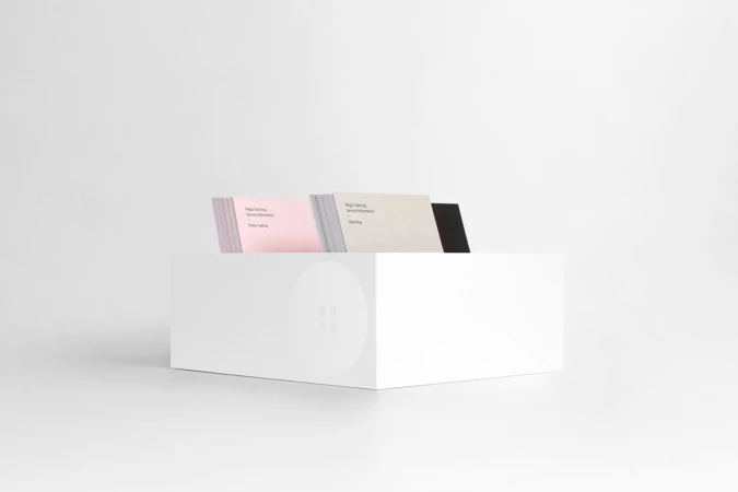 White storage box holding stacked business cards in pink, cream, and black against a white seamless background.