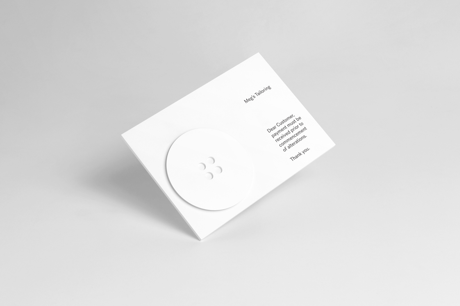 White paper card with minimalist typography and a circular embossed button on a plain grey seamless background.