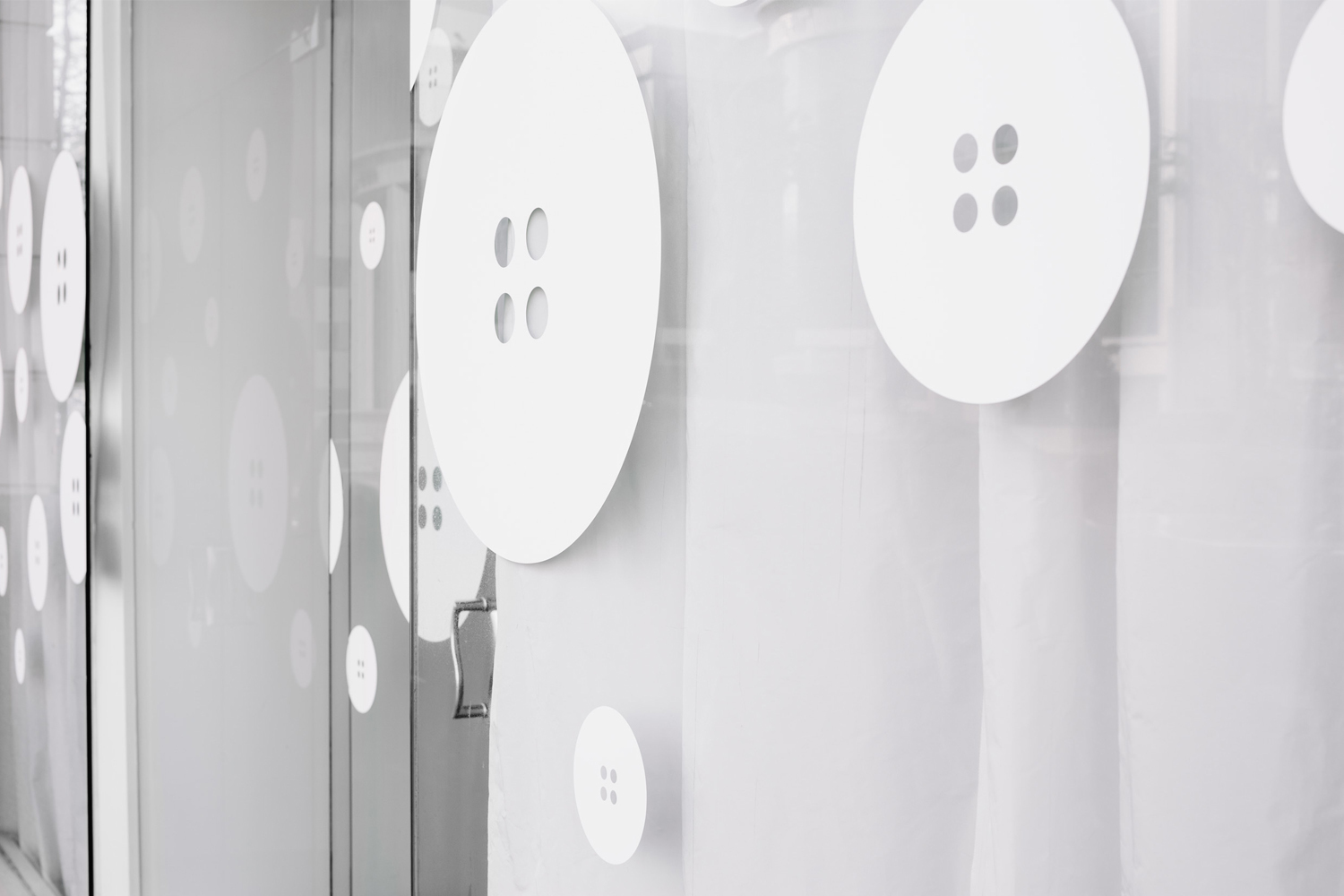 Storefront glass decorated with large white four-hole button decals for Meg's Tailoring brand identity.