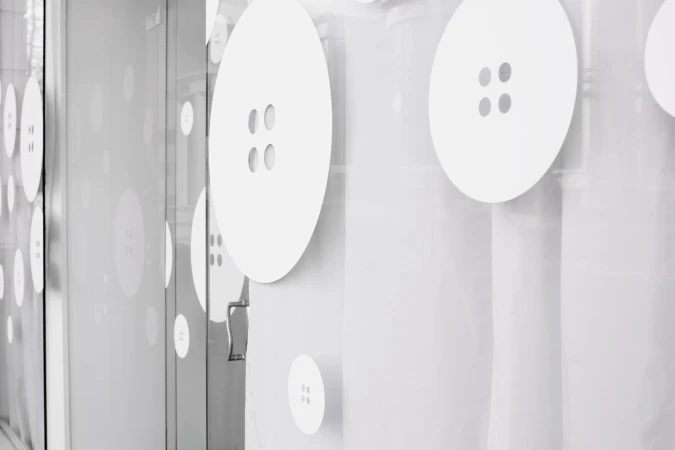 Storefront glass decorated with large white four-hole button decals for Meg's Tailoring brand identity.
