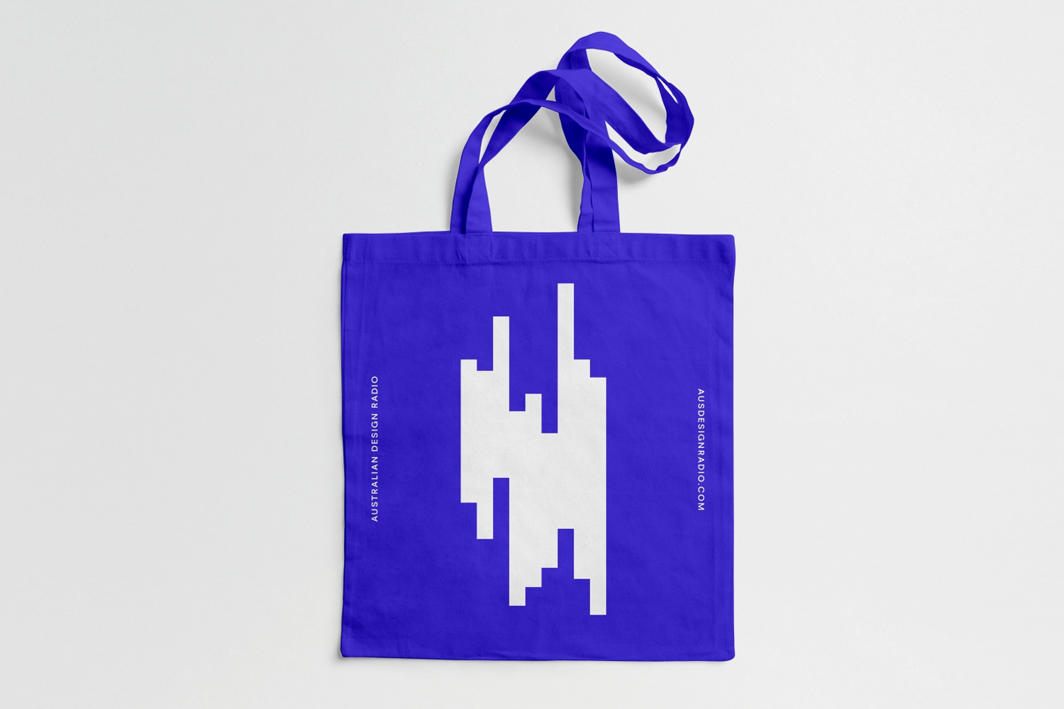 Blue tote bag featuring a white abstract geometric graphic and text on a seamless white background.