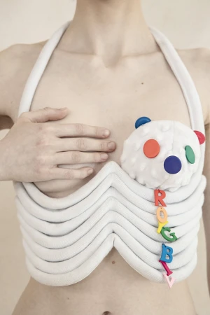 Close-up of a person wearing a white structured sculptural top with a plush toy detail and colorful letter charms.