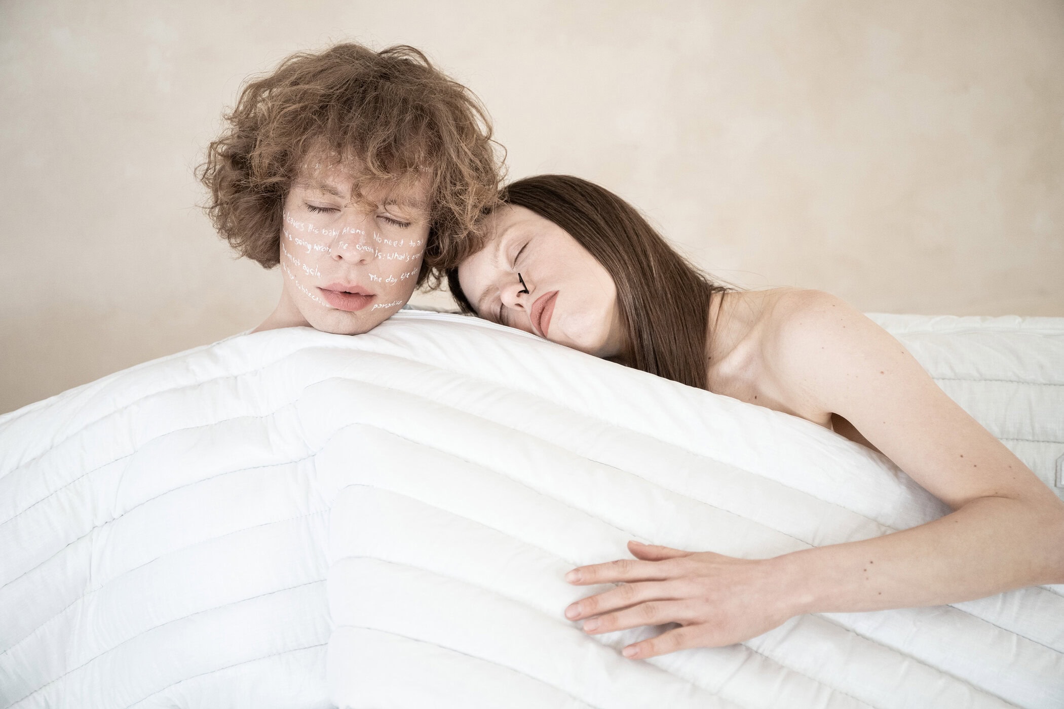 Two models posing closely together wrapped in a white quilted textile against a neutral background.