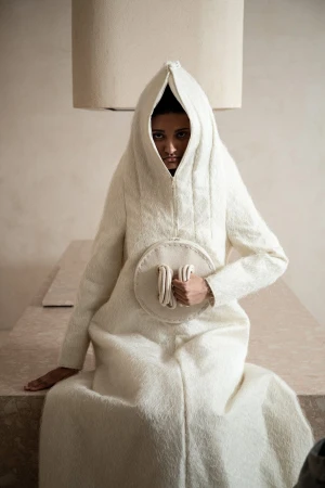 Model wearing a textured white hooded garment holding a round handle for Dzhus Anticon campaign