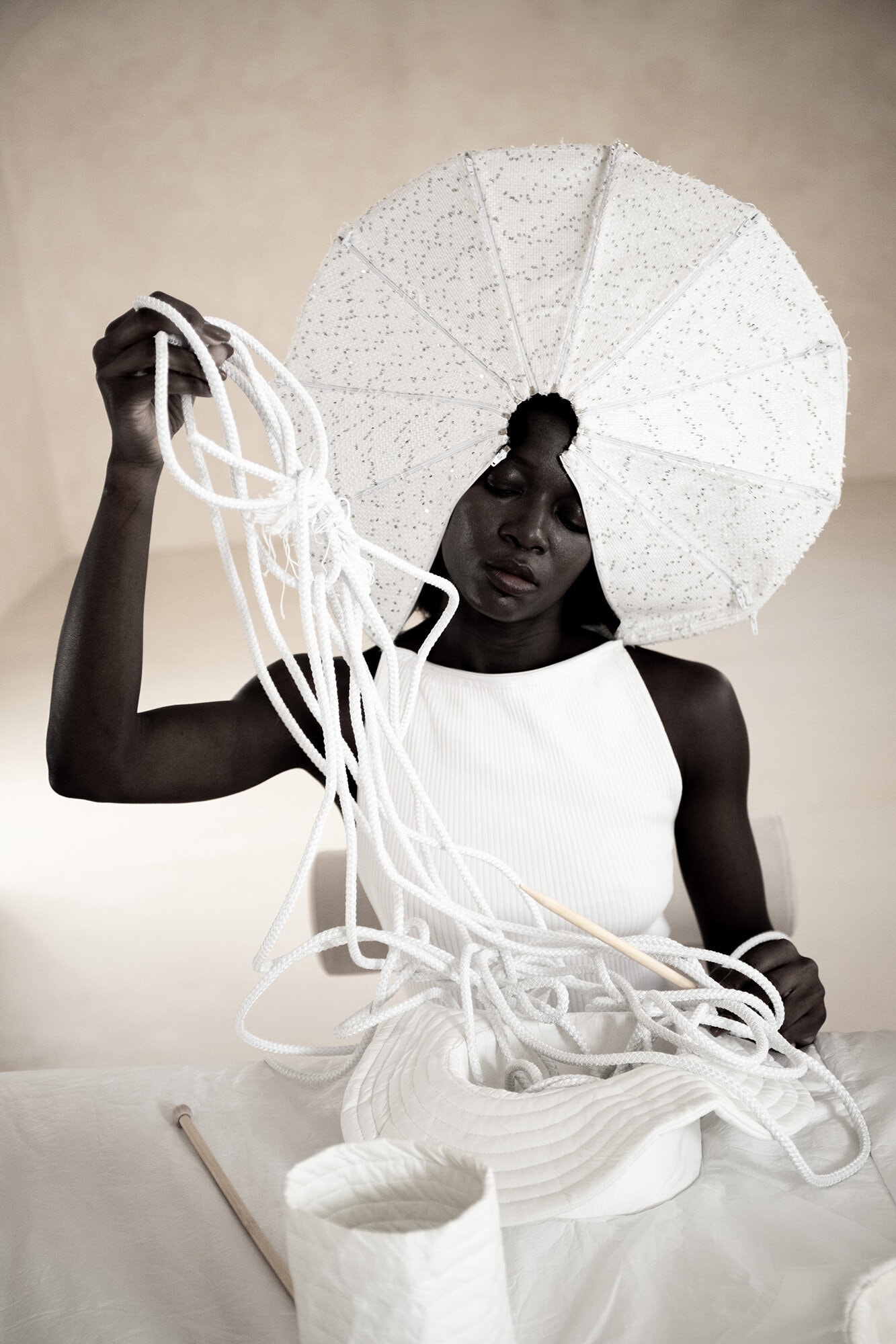 Model wearing sculptural white headdress holding knotted white cords in Dzhus Anticon campaign
