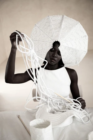 Model wearing sculptural white headdress holding knotted white cords in Dzhus Anticon campaign
