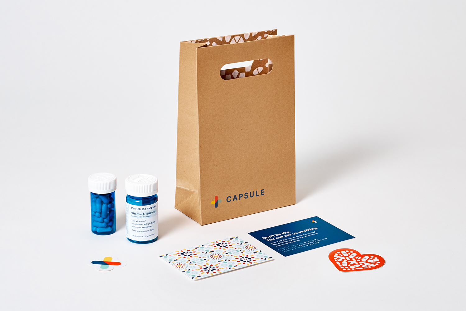 Kraft paper bag with Capsule branding, two small blue pill bottles, printed cards, and stickers on white seamless