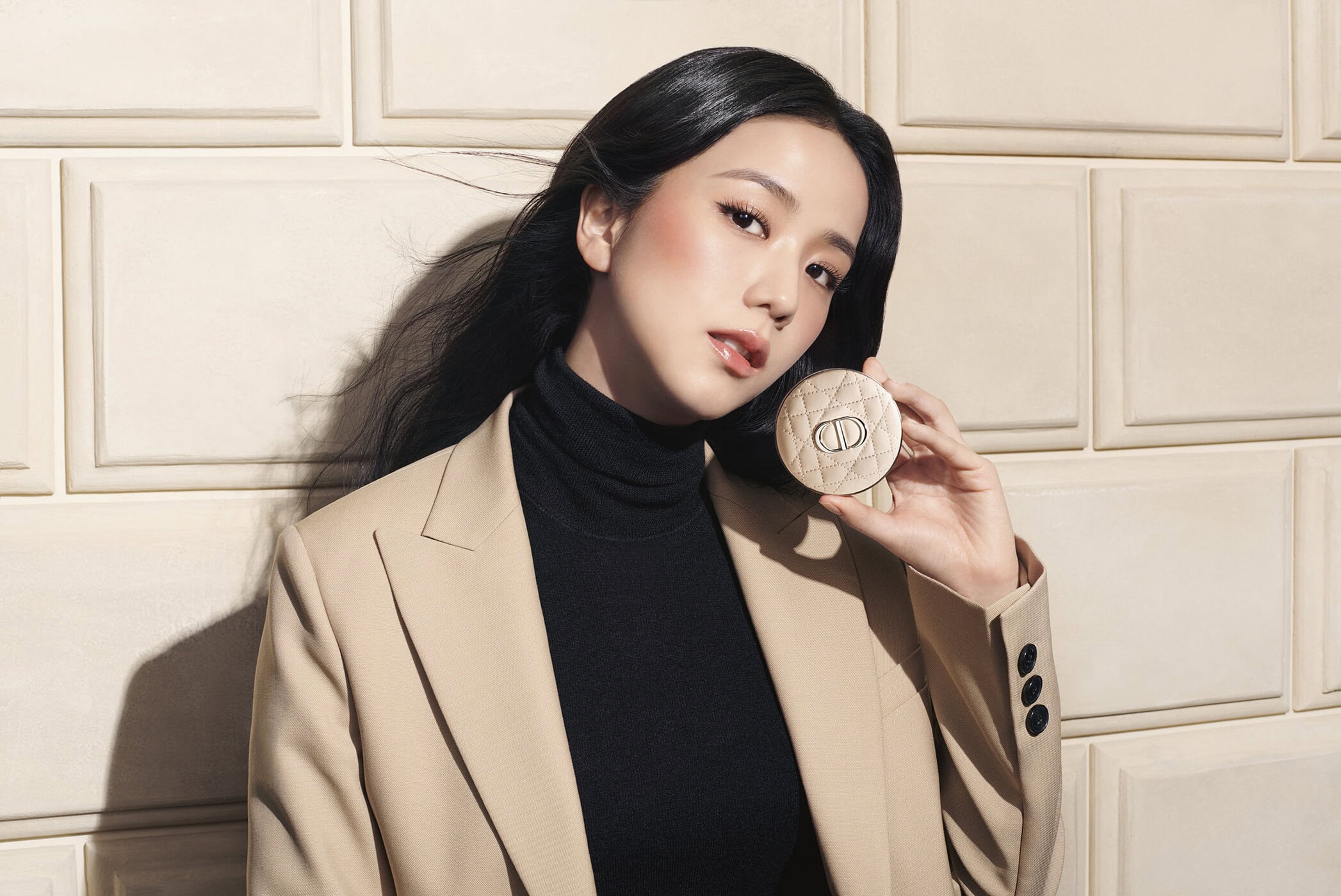 Jisoo holding a round quilted compact against a beige paneled wall for Dior Forever 2025 campaign
