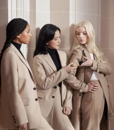 Willow Smith, Jisoo, and Anya Taylor-Joy wearing beige blazers and coats against a neutral architectural pillar background