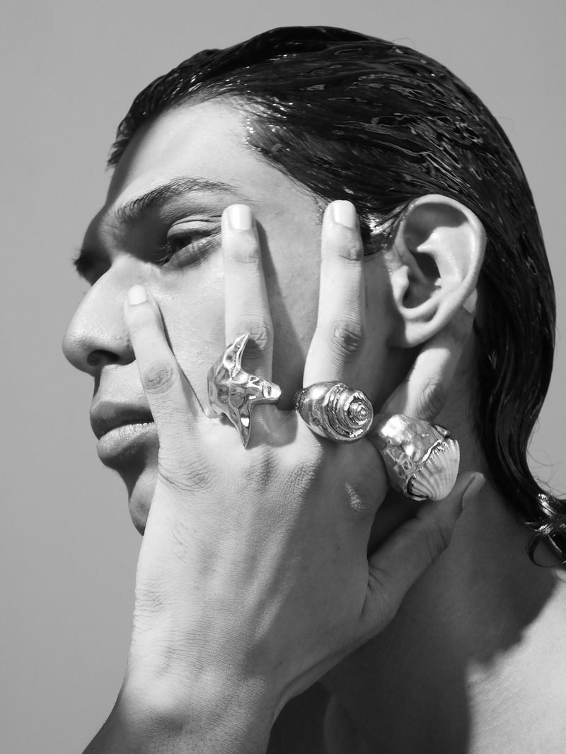 Monochrome portrait of a stylish young adult with three large rings, hand to face in a bright studio setting. Beauty shot.