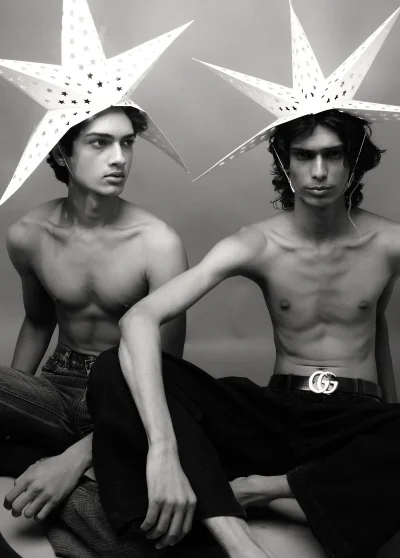 Two shirtless male models wearing large white star-shaped paper headpieces in a studio fashion portrait.