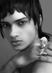 Close-up portrait of a male model wearing sculptural silver rings against a plain studio background.
