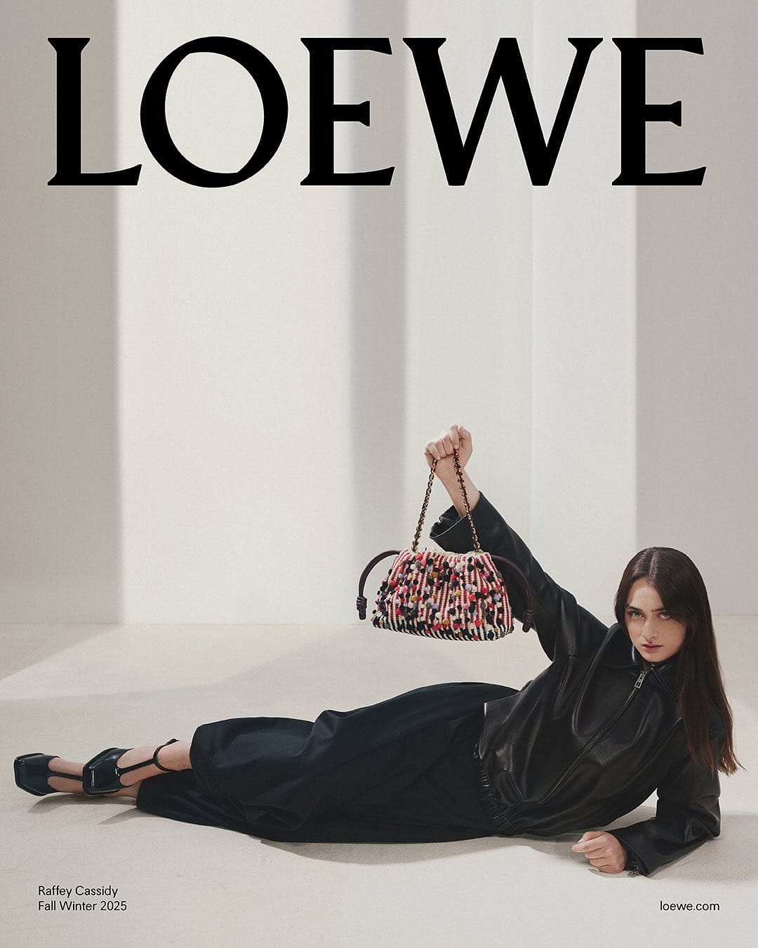 Model Raffey Cassidy in black leather holding a textured patterned handbag for Loewe Fall 2025 ad campaign.