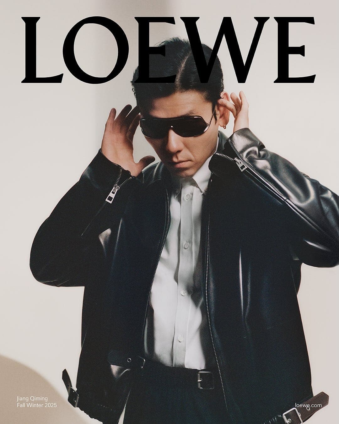 Man wearing dark sunglasses, white shirt, and black leather jacket against a neutral studio background.