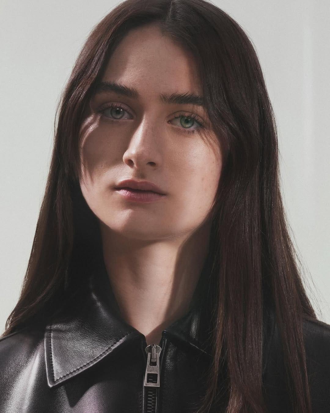 Portrait of a young woman with dark hair wearing a black leather jacket against a light background