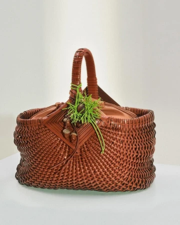 Brown woven leather basket handbag with acorn charms and bright green thread detail on a white background