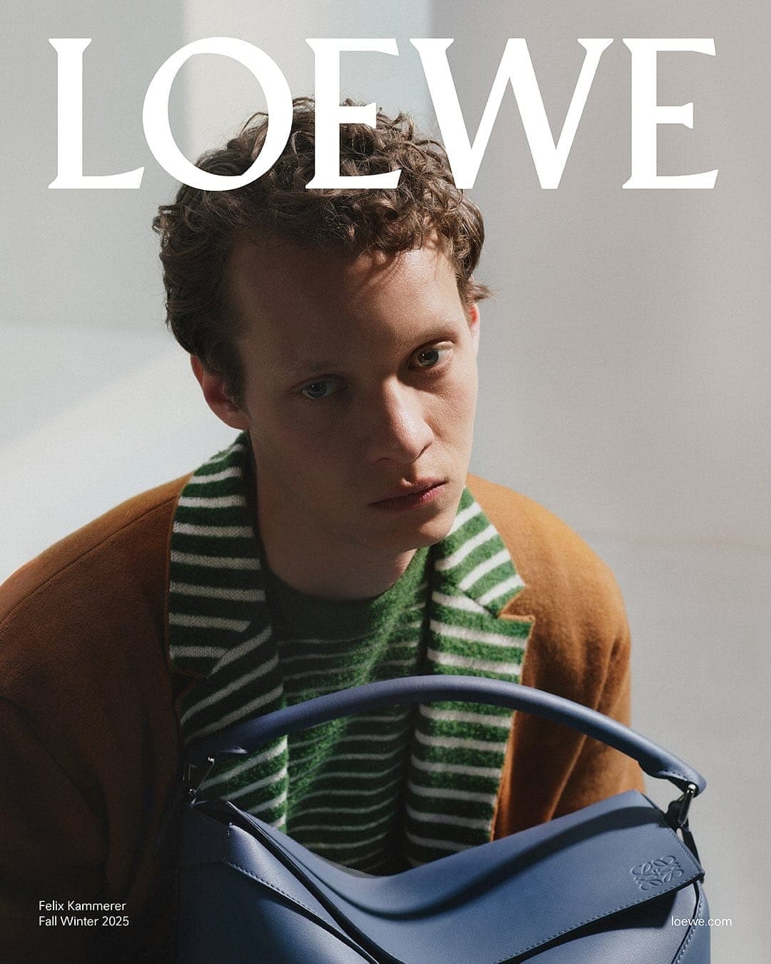 Felix Kammerer wearing a brown jacket and green striped sweater holding a blue leather handbag for Loewe