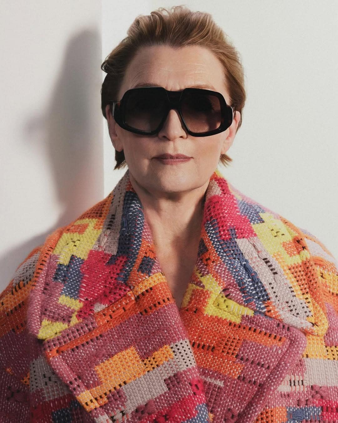 Lesley Manville wearing dark oversized sunglasses and a colourful knit coat against a white background for Loewe.