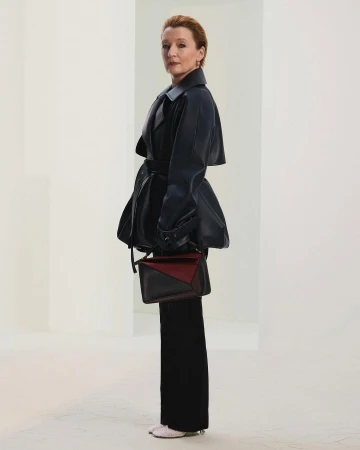 Lesley Manville wearing dark coat and holding a color-blocked handbag in a minimalist white architectural interior for Loewe Fall 2025 ad campaign