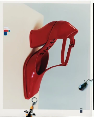 Glossy red T-bar high heel shoe on a cream and white background with small dangling charms.