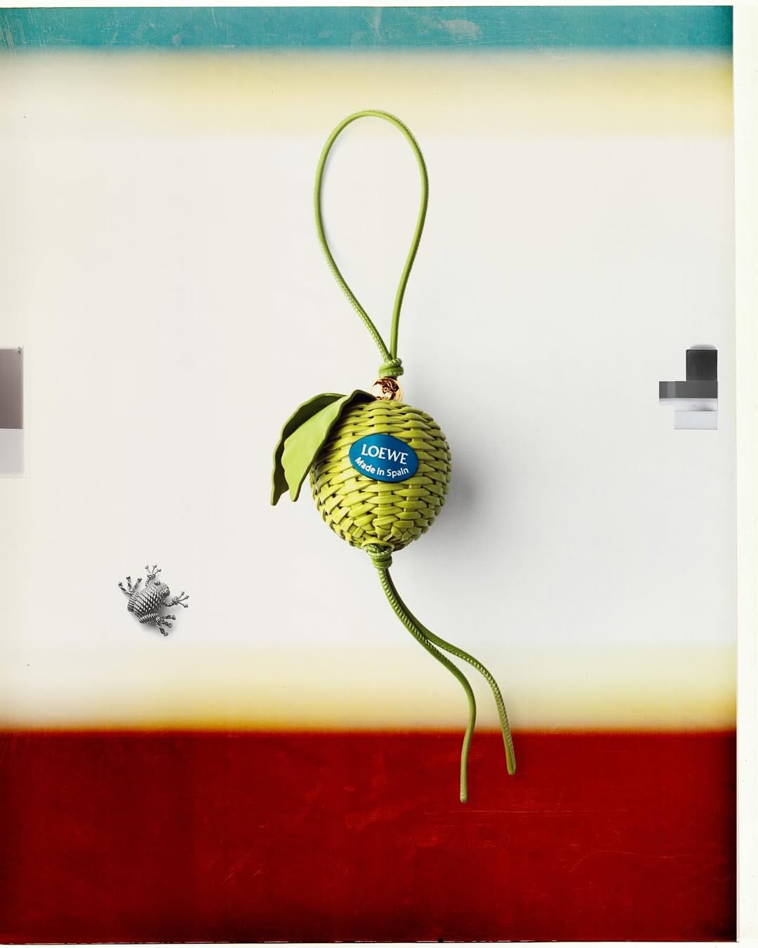 Woven green leather fruit charm featuring a blue brand label suspended against a white and red background.