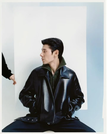 Man wearing a black leather jacket and olive green collar against a white and pale blue studio backdrop