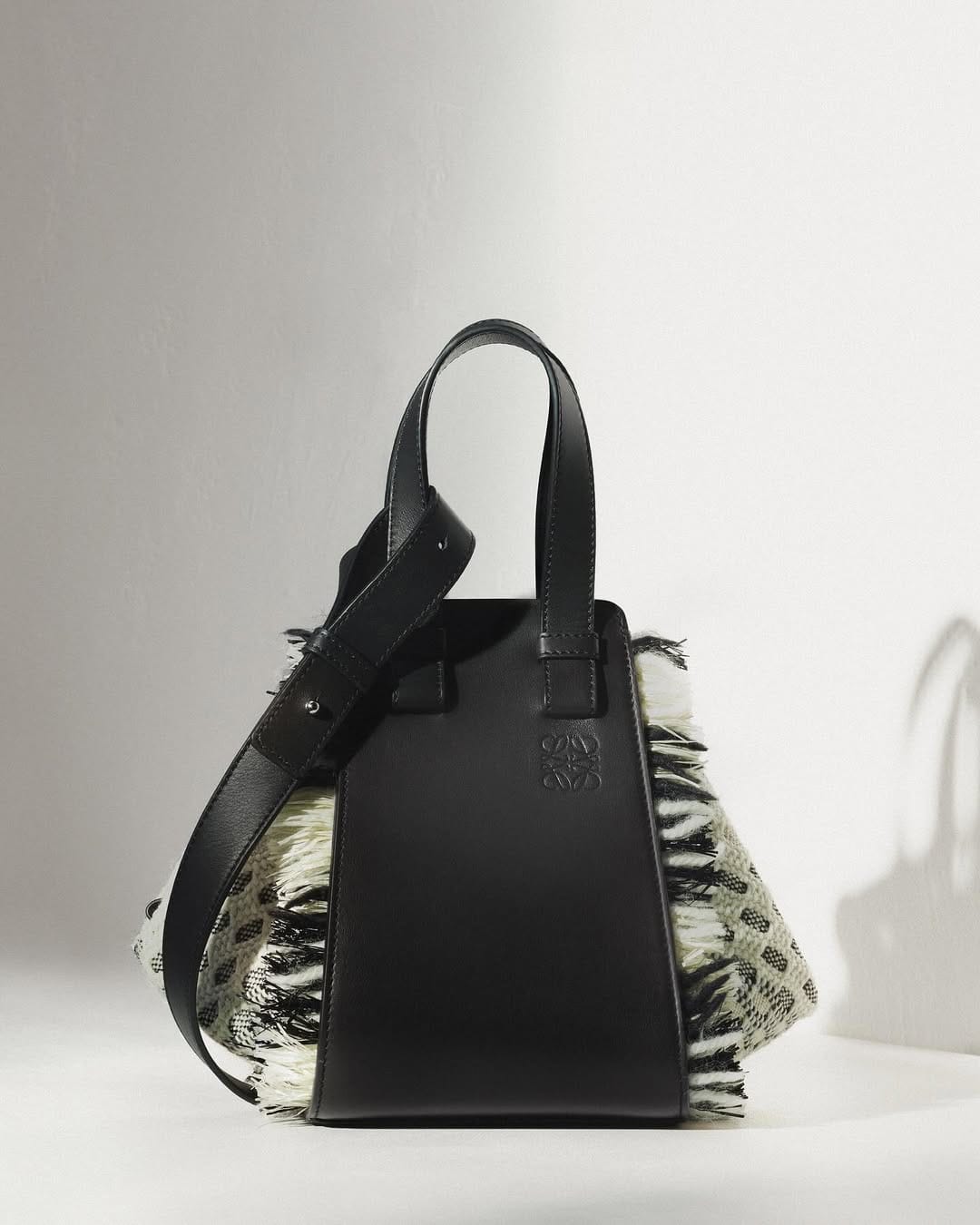 A black leather handbag with textured fringe side panels displayed against a white background