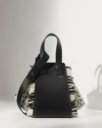 A black leather handbag with textured fringe side panels displayed against a white background