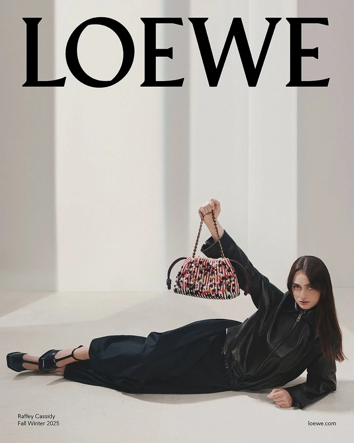 Model Raffey Cassidy in black leather holding a textured patterned handbag for Loewe Fall 2025 ad campaign.