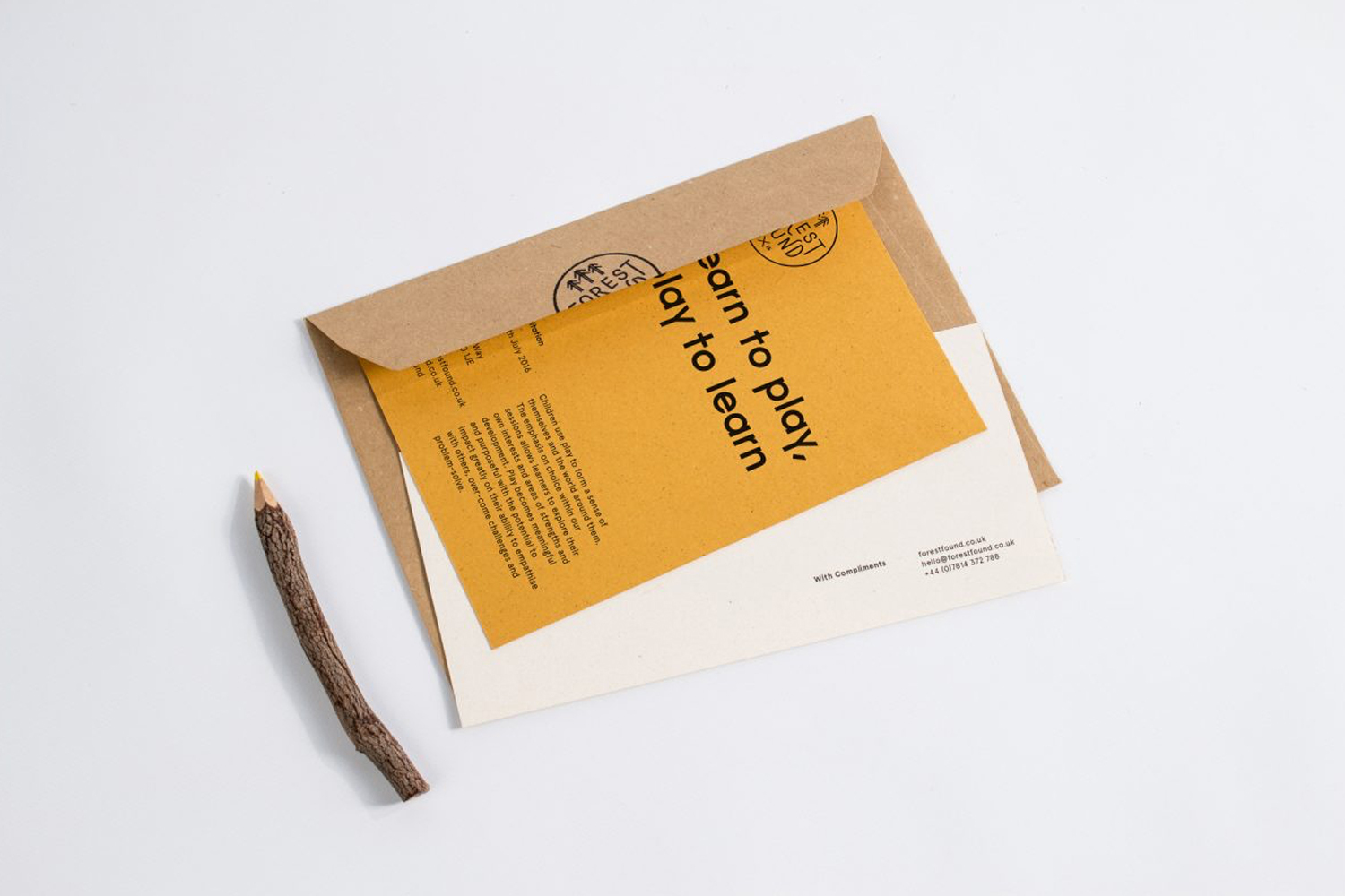 Craft paper envelope with a yellow insert card and a wooden twig pencil on a clean white surface