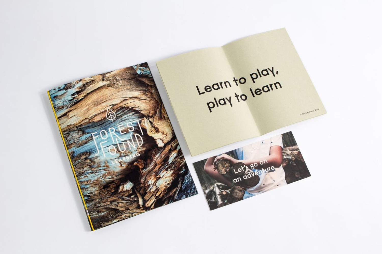 Printed booklet, open book with typography, and postcard laid out on a white surface.