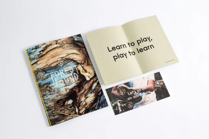 Printed booklet, open book with typography, and postcard laid out on a white surface.