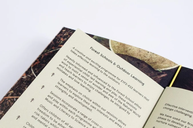 Close-up of an open printed booklet displaying typographic text on cream paper against a plain white background