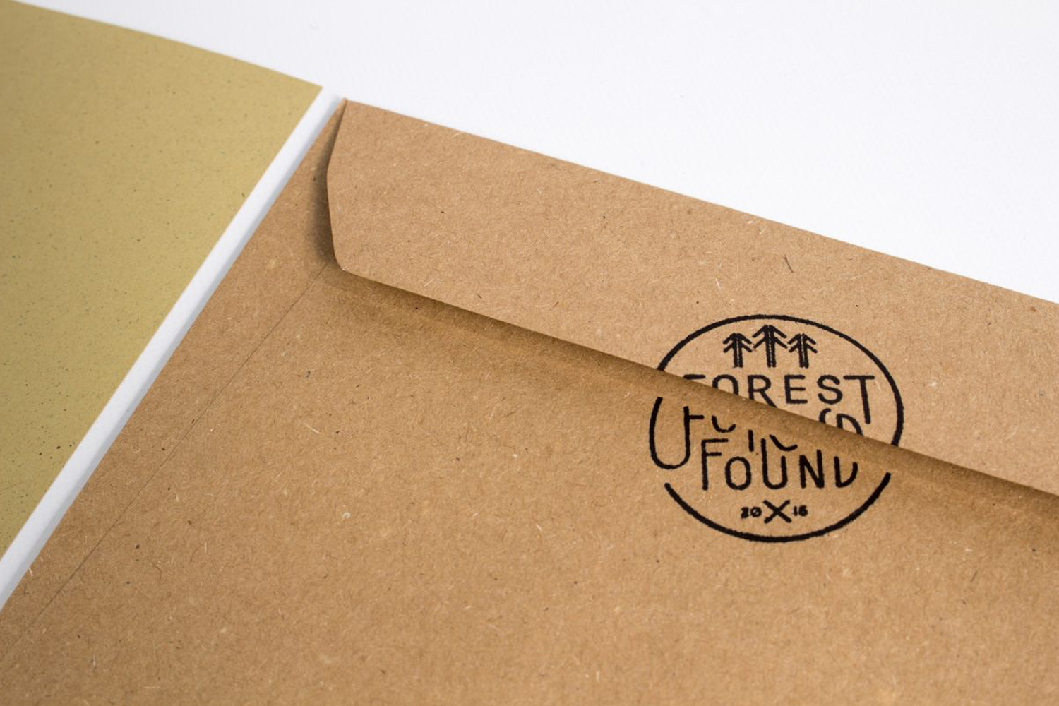 Kraft paper envelope with a black circular Forest Found logo stamp resting on a white surface.