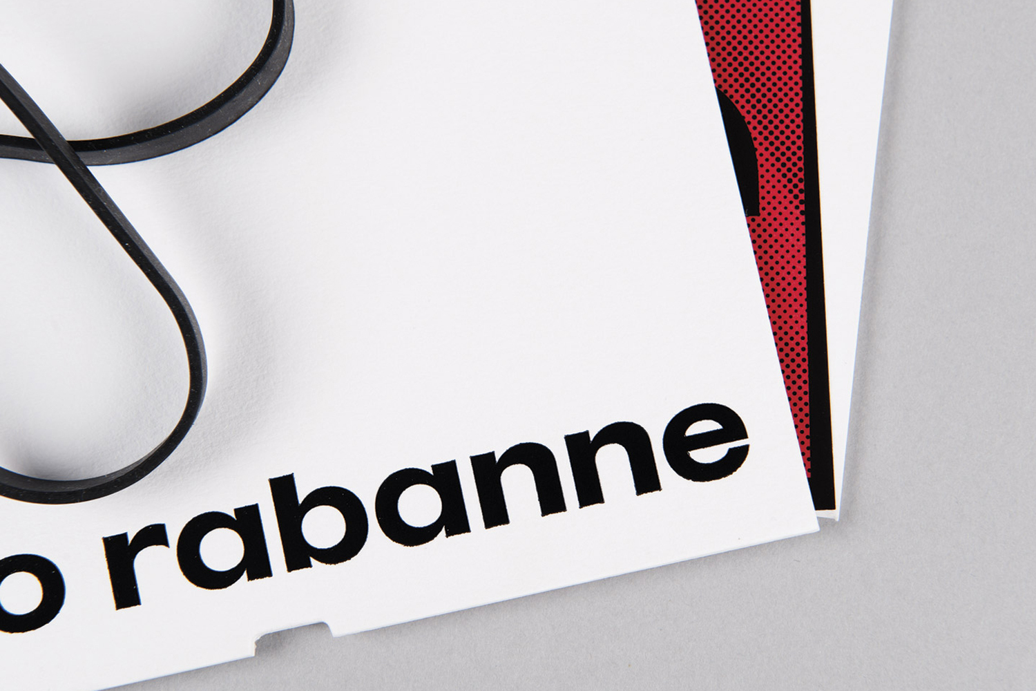 Close-up of Paco Rabanne brand identity stationery with bold black typography on white paper and a black rubber band.