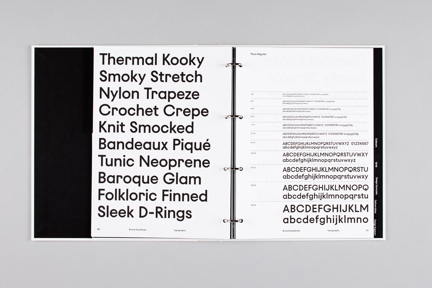 An open ring binder brand guidelines document showcasing bold sans-serif typography and layout grids on a grey surface.