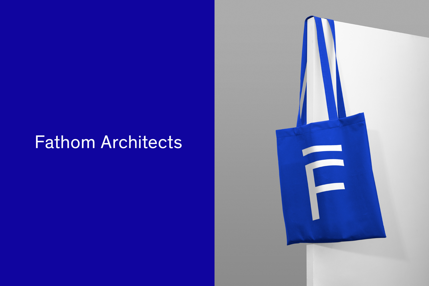 Blue tote bag featuring a white Fathom Architects logo hanging against a grey wall next to a solid blue panel with white text