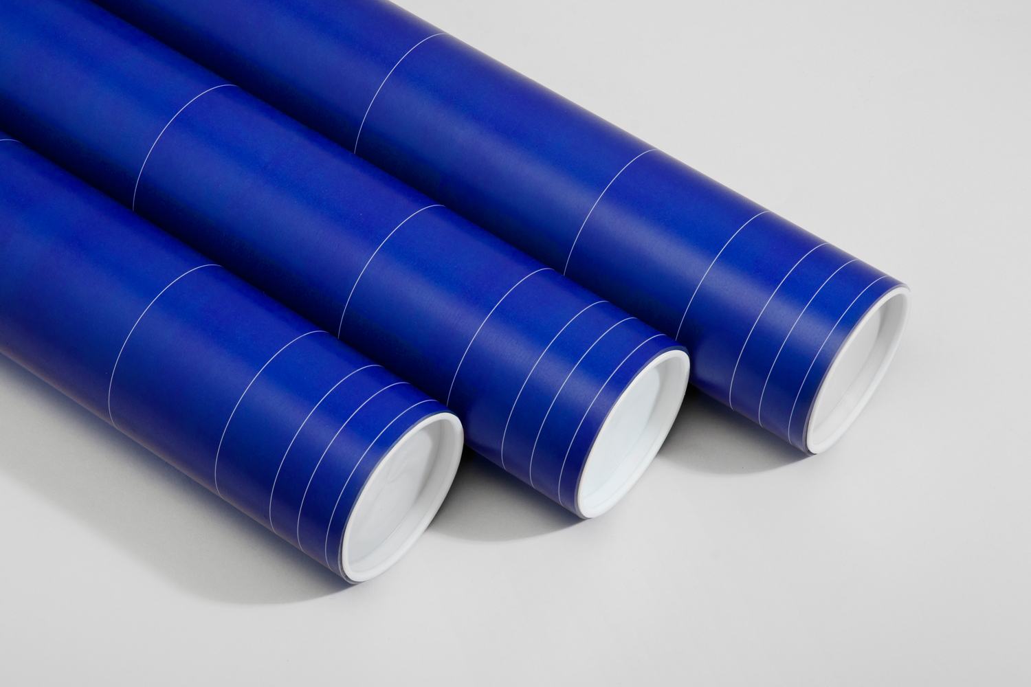 Three blue architectural tubes with white ring markings resting diagonally on a pale grey studio surface.
