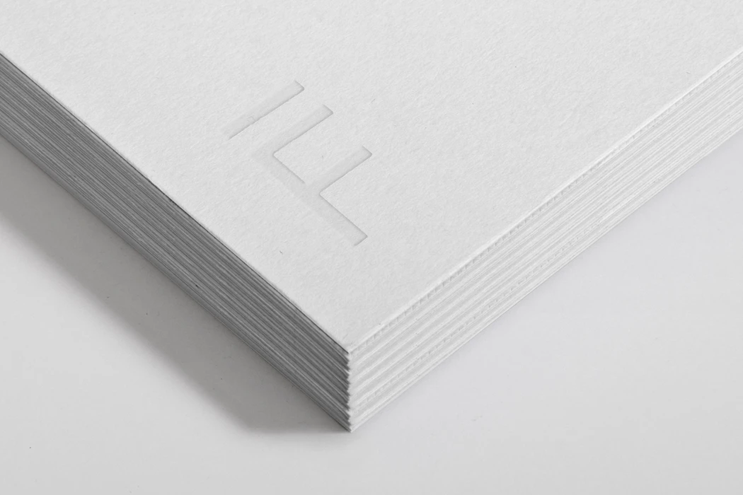Close-up of a thick stack of white textured paper with an embossed architectural logo on top