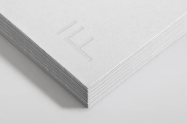 Close-up of a thick stack of white textured paper with an embossed architectural logo on top
