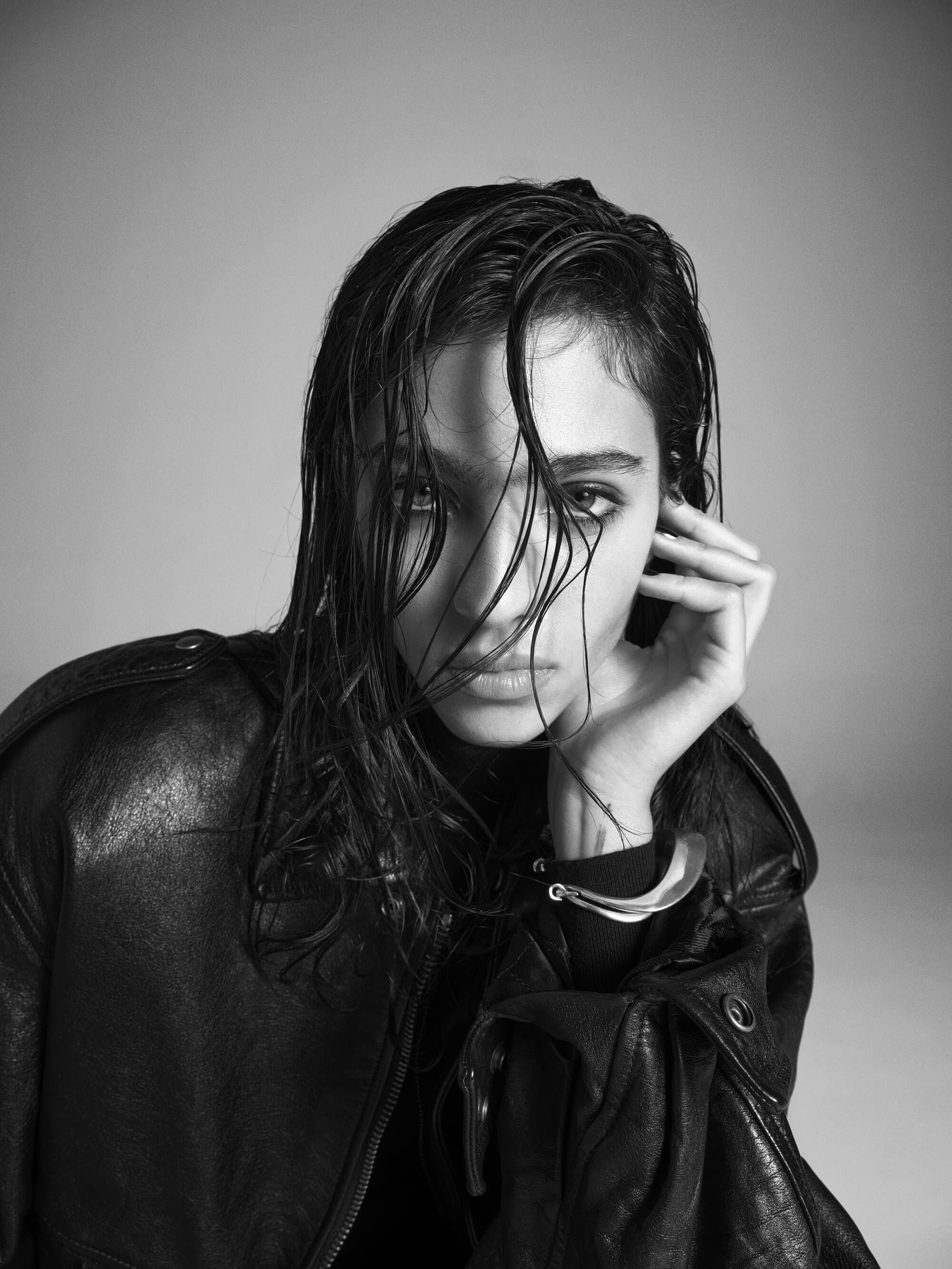 Model with wet hair in a black leather jacket against a grey studio background